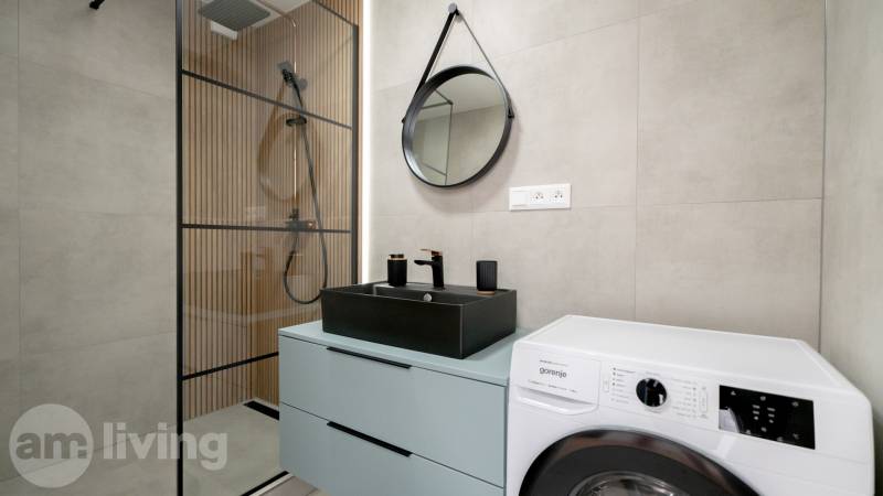 A bathroom with a shower, washing machine, and sink in a 2-room apartment.