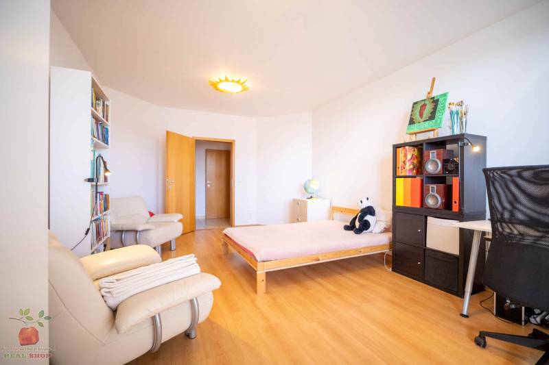 A bright room with wooden flooring in a 3-room apartment, containing a bed and a bookshelf.