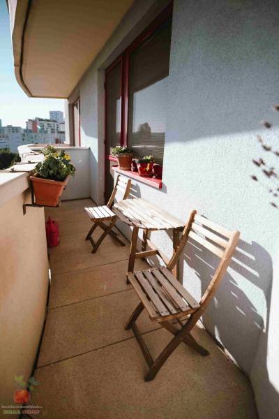 A balcony of a 3-room apartment with wooden furniture and flower pots.