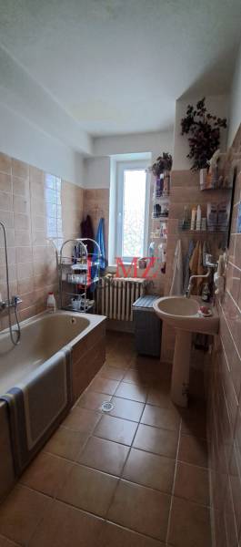 A bathroom in a family house with light tiles, a bathtub, and a sink.