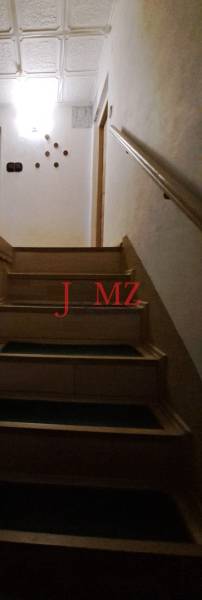 A staircase with a wooden railing in a family house, illuminated by a ceiling light.