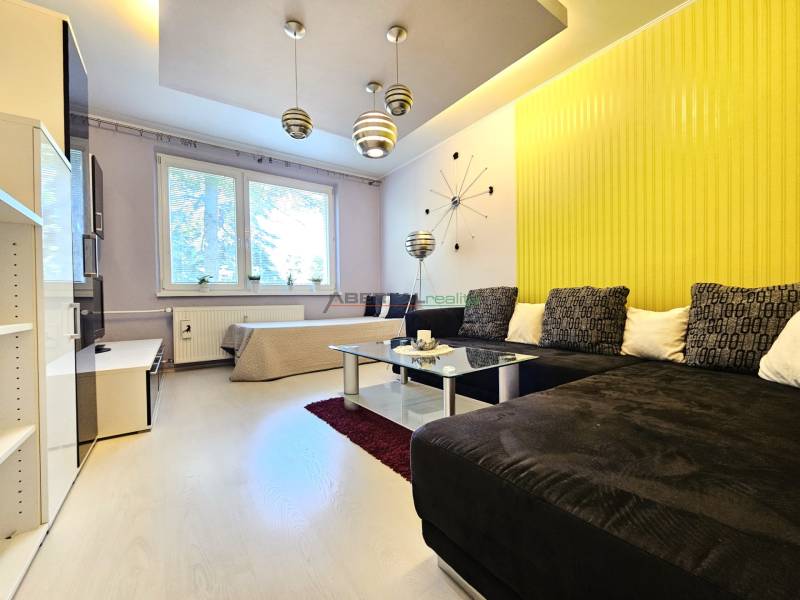 Living room in a two-room apartment with a yellow wall, brown sofa, and modern chandelier.