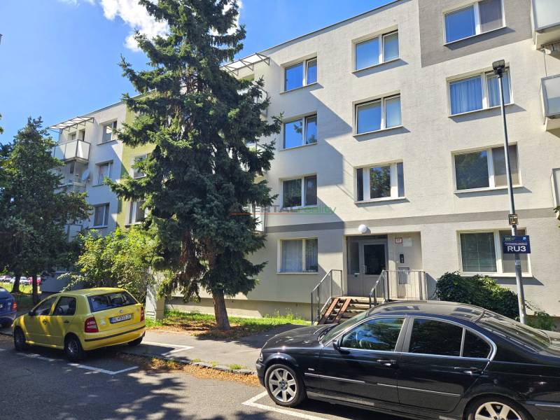 An apartment building in Bratislava on Nezábudkova Street among trees and parked cars.