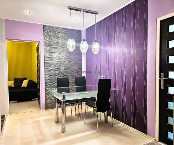 Dining area in a 2-room apartment with purple walls and a glass table.