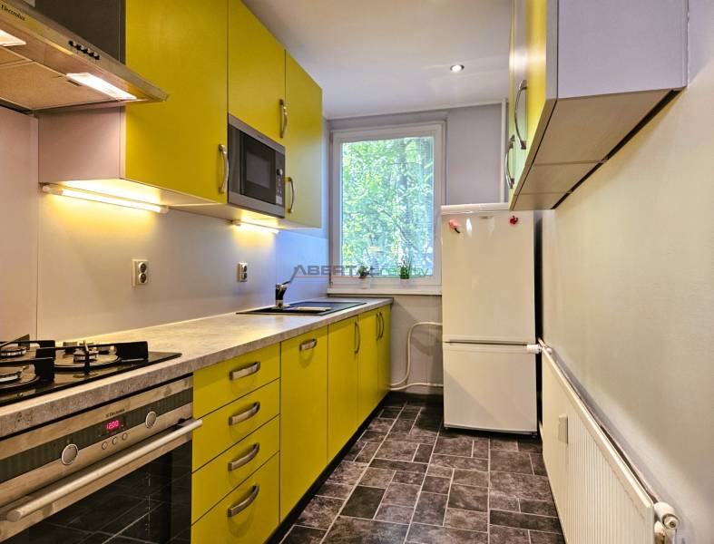 A kitchen in a 2-room apartment with yellow cabinets, a white refrigerator, and a stove.