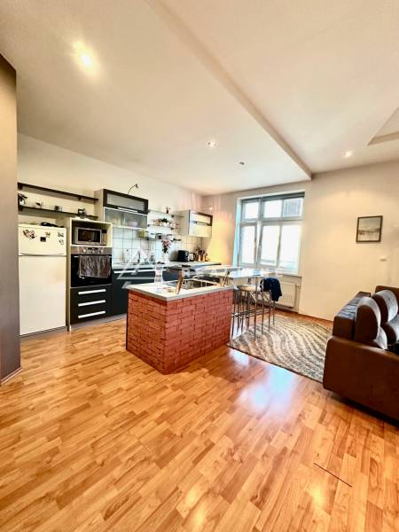 A kitchen with a bar counter and wooden flooring in a 2-room apartment.