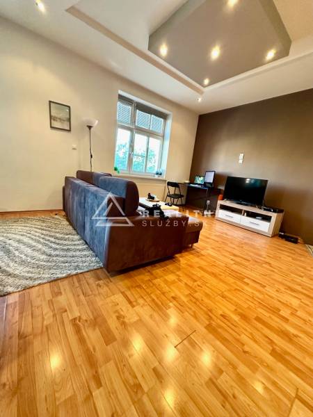 Living room in a two-room apartment with a sofa and a television, wooden floor and white walls.