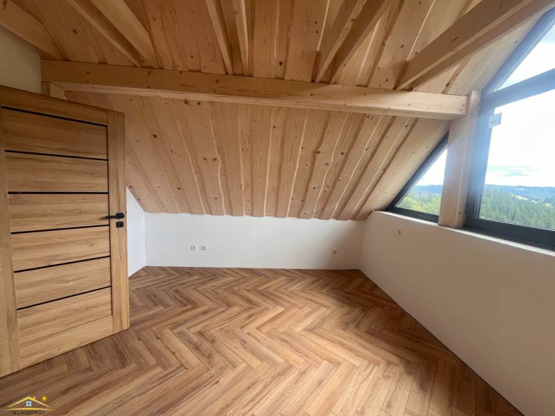 Attic room in a cottage with a wooden ceiling, large window, and parquet floor.