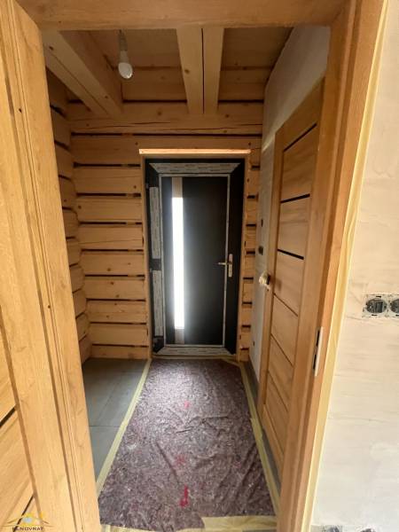 A wooden hallway in a cabin with dark doors and an exposed light bulb on the ceiling.