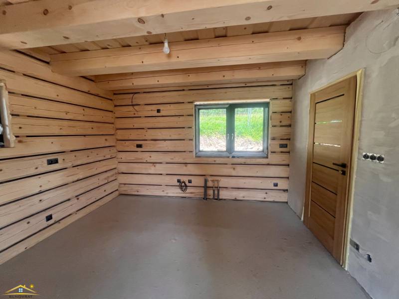 The interior of a cabin with wooden walls, a window, and simple lighting.