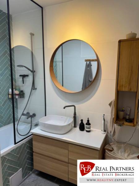 A bathroom in a 4-room apartment with a wooden sink and a round mirror.