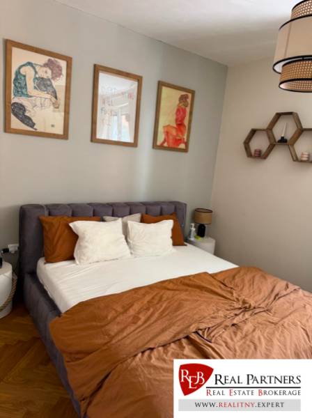 Bedroom in a 4-room apartment with a large bed, pictures, and brown quilted bedding.