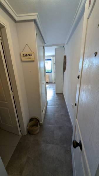 A narrow hallway in a studio apartment with baskets on the floor leads to a window.