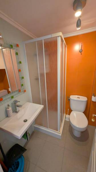 A studio apartment bathroom with orange tiles, a shower, a toilet, and a sink.