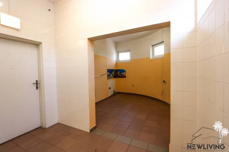 Commercial space with white tiles, bright lighting, and orange interior walls.