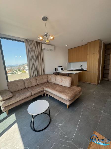 Living room of a holiday apartment with a corner sofa, view, and kitchenette.