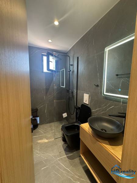 Bathroom of the recreational apartment with a shower, black sink, and illuminated mirror.
