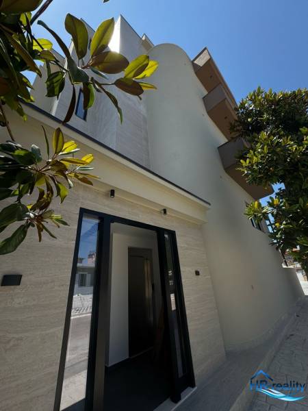 The facade of a holiday apartment in Ksamil, surrounded by greenery and a clear sky.