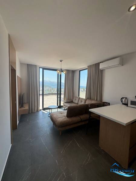 Living room in a holiday apartment with large windows, a sofa, and a kitchenette.