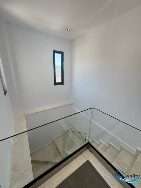 Staircase in a recreational apartment with large glass railing and narrow window.