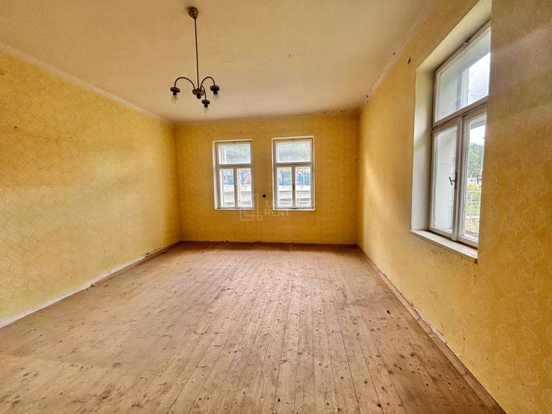 A room in a family house with a wooden floor, yellow walls, and a pendant light.