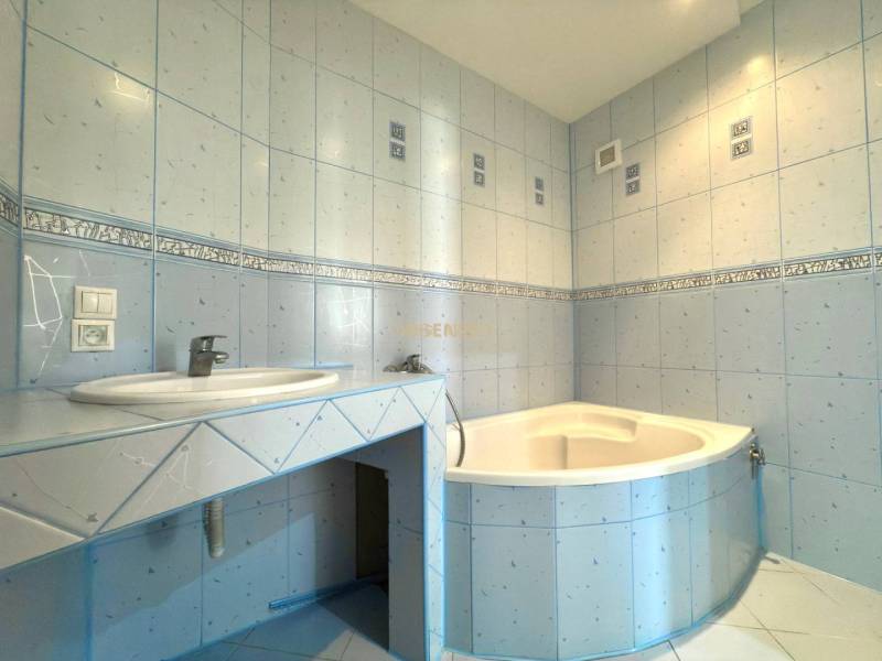 A bathroom with light blue tiles and a corner bathtub in a 4-room apartment.