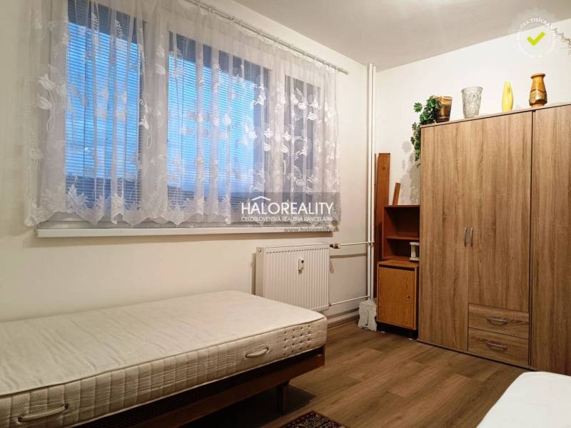 The room offers a simple bed and a wooden wardrobe in a 2-room apartment.