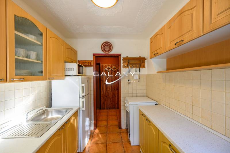 A kitchen in a cottage with wooden cabinets and appliances, warm tiles on the floor.