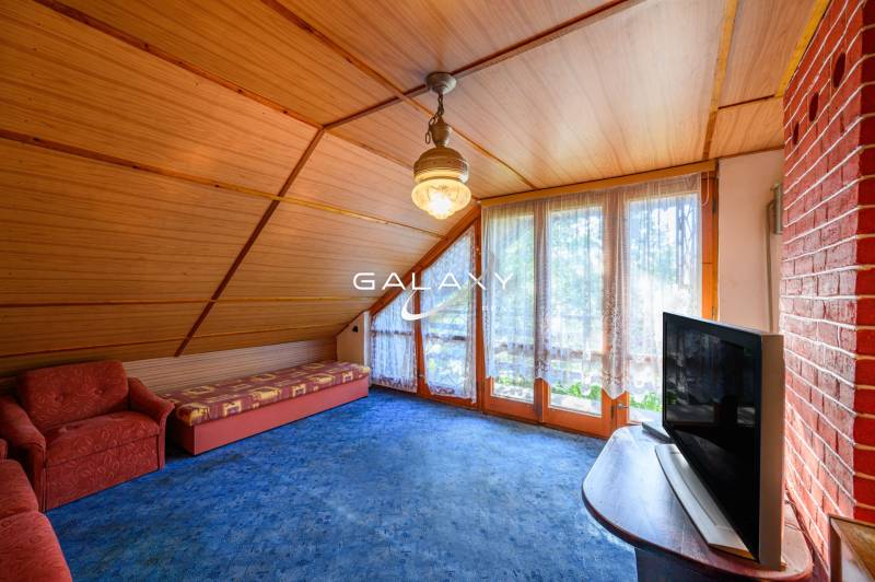 Cozy space in a cabin with an armchair, sofa, TV, and large windows with a view.
