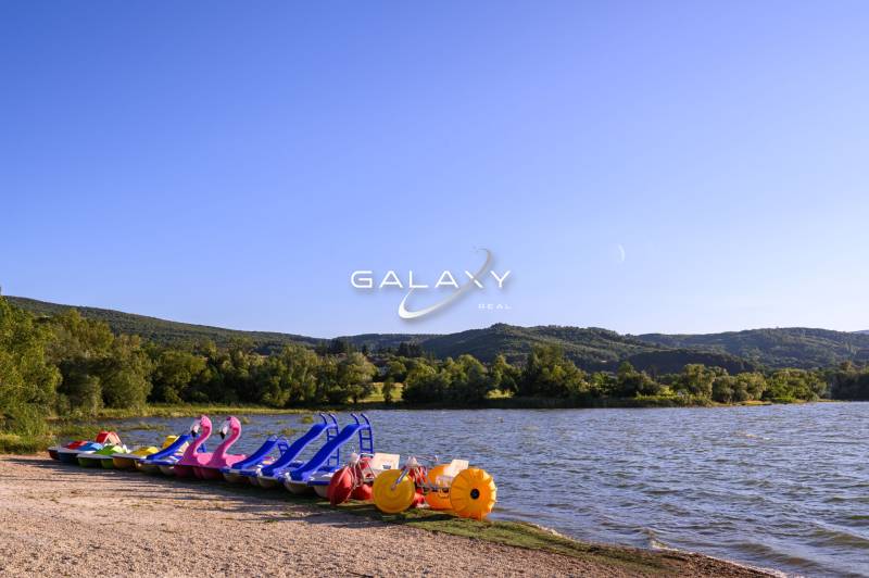 Pedal boats at the lake in Ružiná surrounded by greenery and hills under a blue sky.
