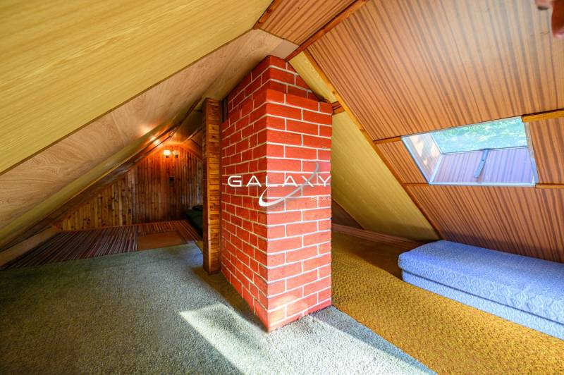 In the attic of a cottage with a brick chimney and a window overlooking the roof.
