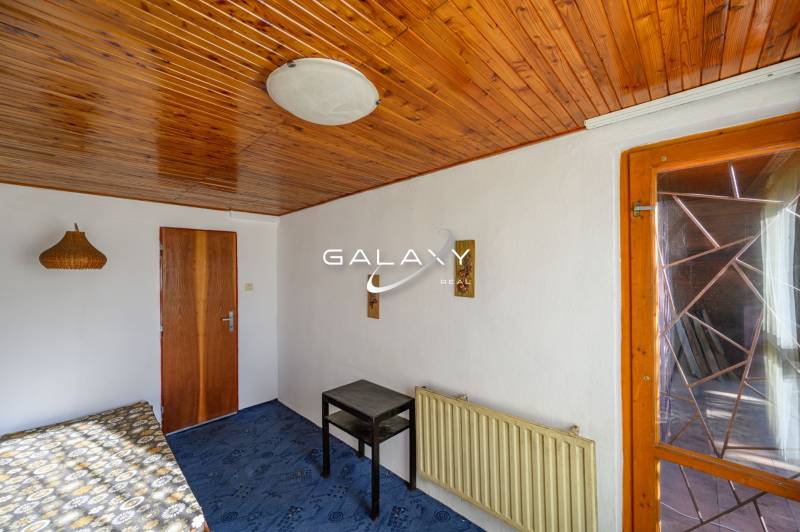 Wooden ceiling, bed, table, blue carpet, lamp on the wall in the cabin.