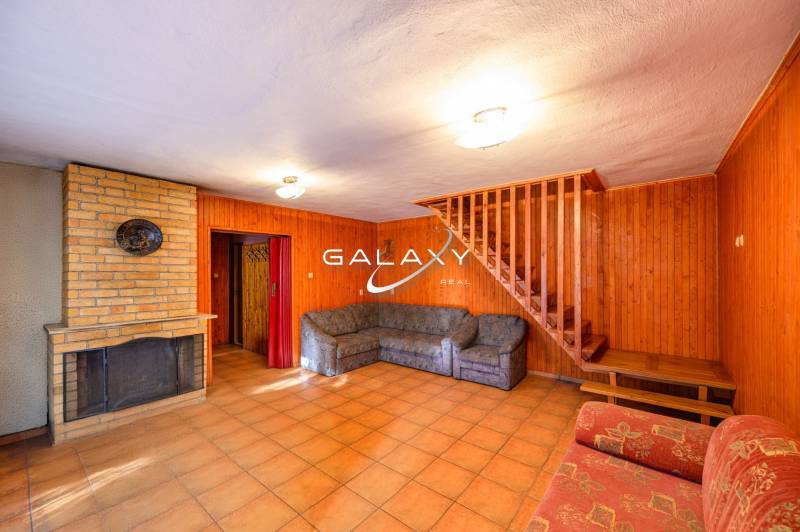 Interior of a cabin with a brick fireplace, wooden paneling, and a staircase.