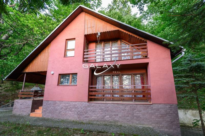 A wooden cottage in Ružiná, surrounded by greenery and with a terrace on the upper floor.