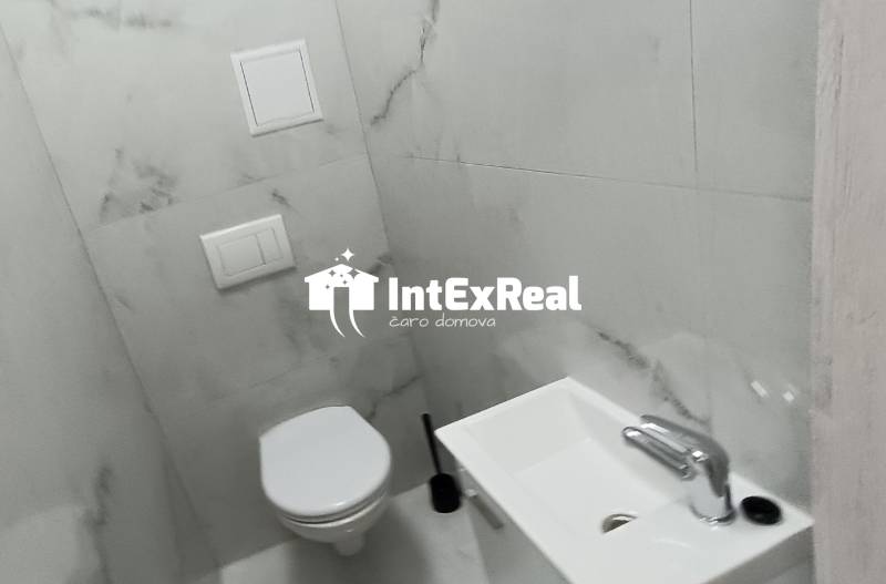 A toilet with a sink and marble walls in a 2-room apartment.