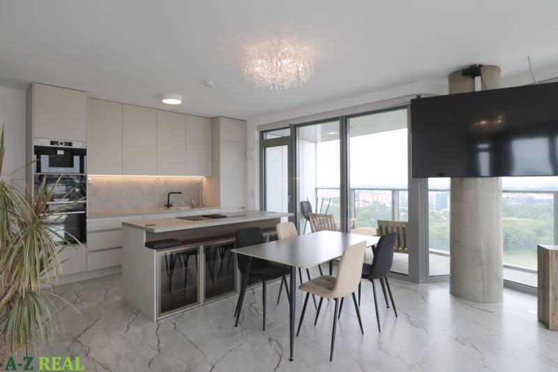 A kitchen in a 3-room apartment with a dining table, wood-patterned flooring, and large windows.