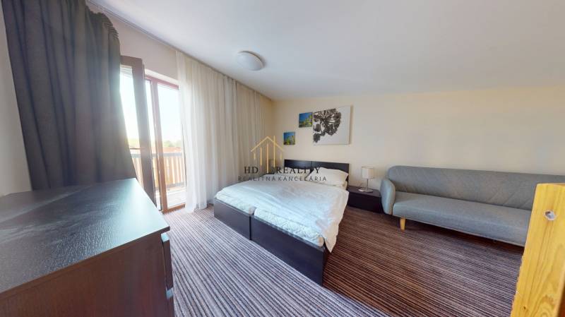 A bedroom in a 2-room apartment with a bed, a couch, and a balcony.