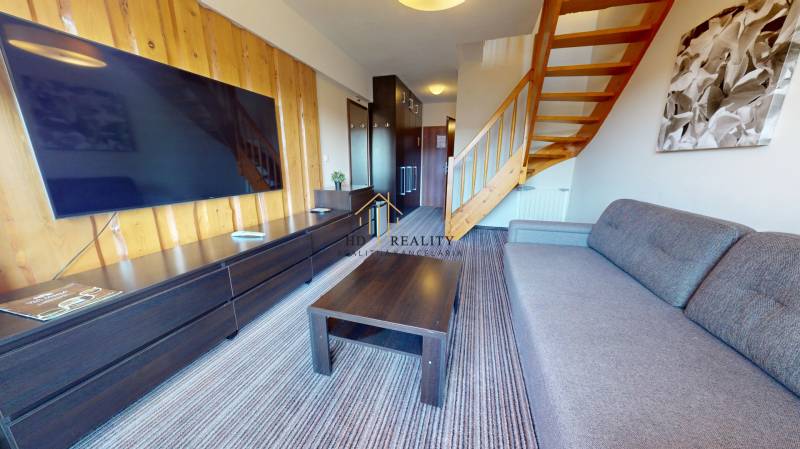 Living room in a 2-room apartment with a staircase and a television on a wooden wall.