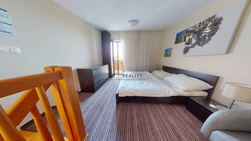 Bedroom in a 2-room apartment with a staircase, a large bed, and photographs on the wall.