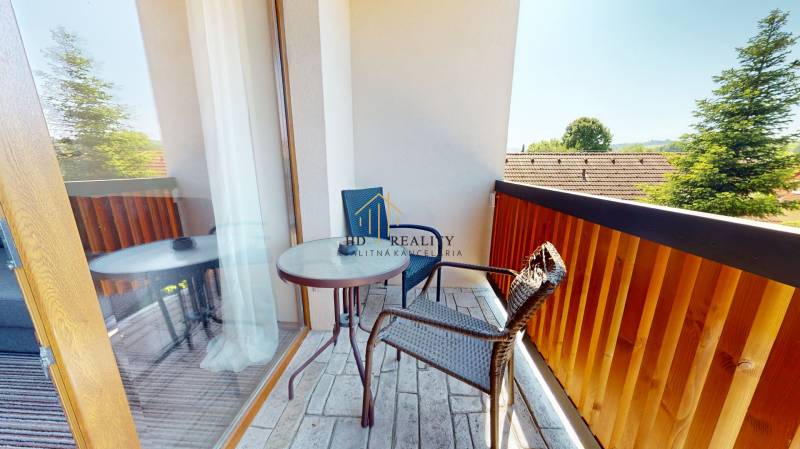 A balcony in a 2-room apartment with a view of the surrounding greenery and rooftops.