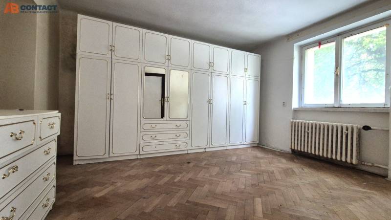 A room of a three-room apartment with a white built-in wardrobe and wooden flooring.