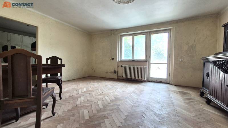 A room in a 3-room apartment with a wooden floor, old furniture, and a large window.