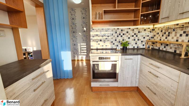 A kitchen in a studio apartment with wooden cabinets and mosaic tiles on the wall.