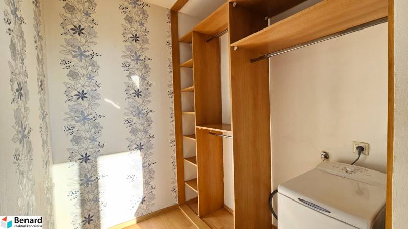 Wardrobe space with wooden shelves and a washing machine in a studio apartment.