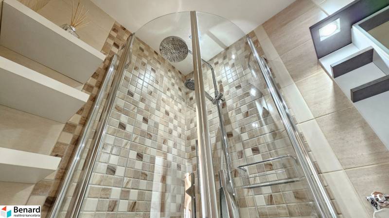 Modern shower cabin with mosaic tiles and shelves in a studio apartment.