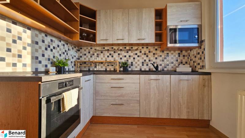 Kitchen in a studio apartment with light wood, built-in oven, and microwave.