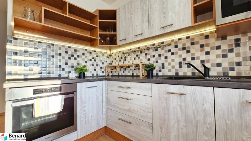 Kitchen in a studio apartment with wooden cabinets, tiles, and an oven.