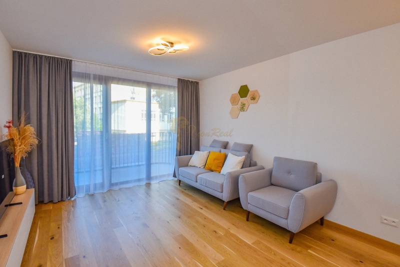 Living room with wooden flooring, gray furniture, and a large window in a three-room apartment.
