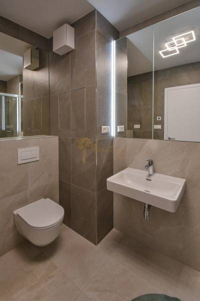 A bathroom with a wall-mounted toilet, sink, and shower in a 3-room apartment.