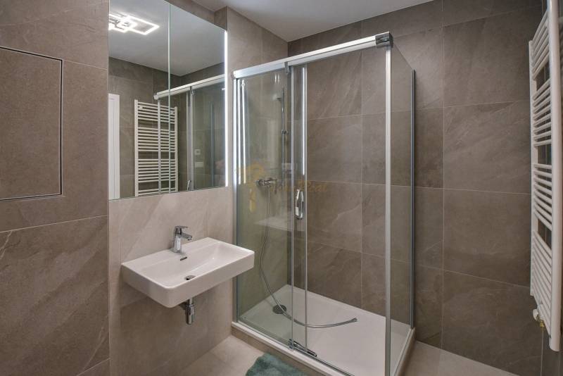 A bathroom in a 3-room apartment with a sink, shower, and mirror with tiles.